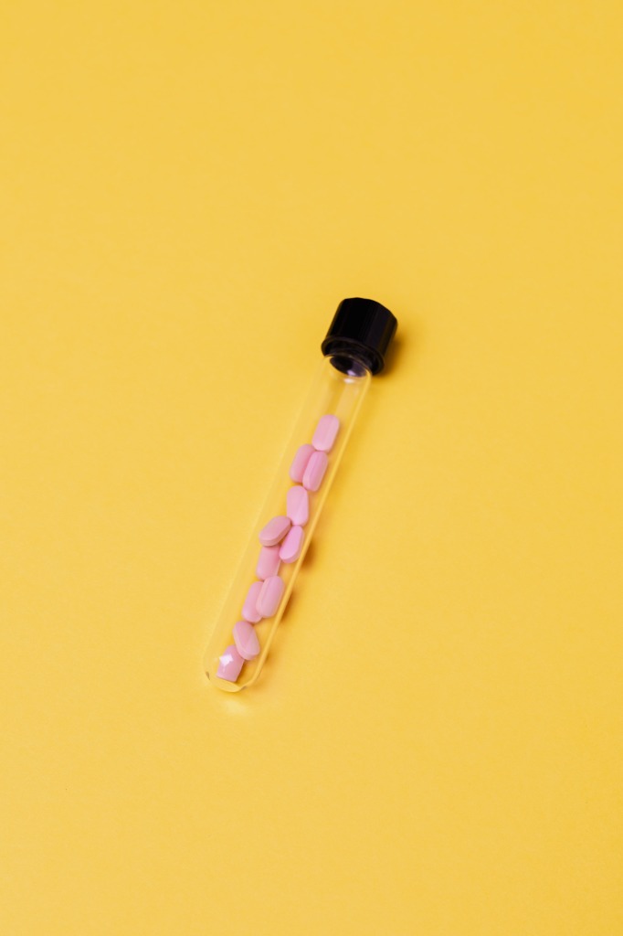 A glass test tube containing pink hormone replacement pills on a clean yellow background