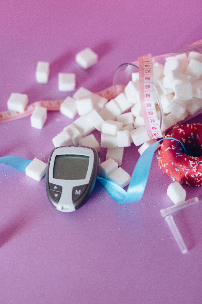 Blood sugar meter, sugar cubes, donut, and measuring tape on a pink background