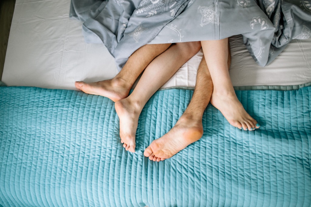 Two pairs of feet under a blanket on a bed