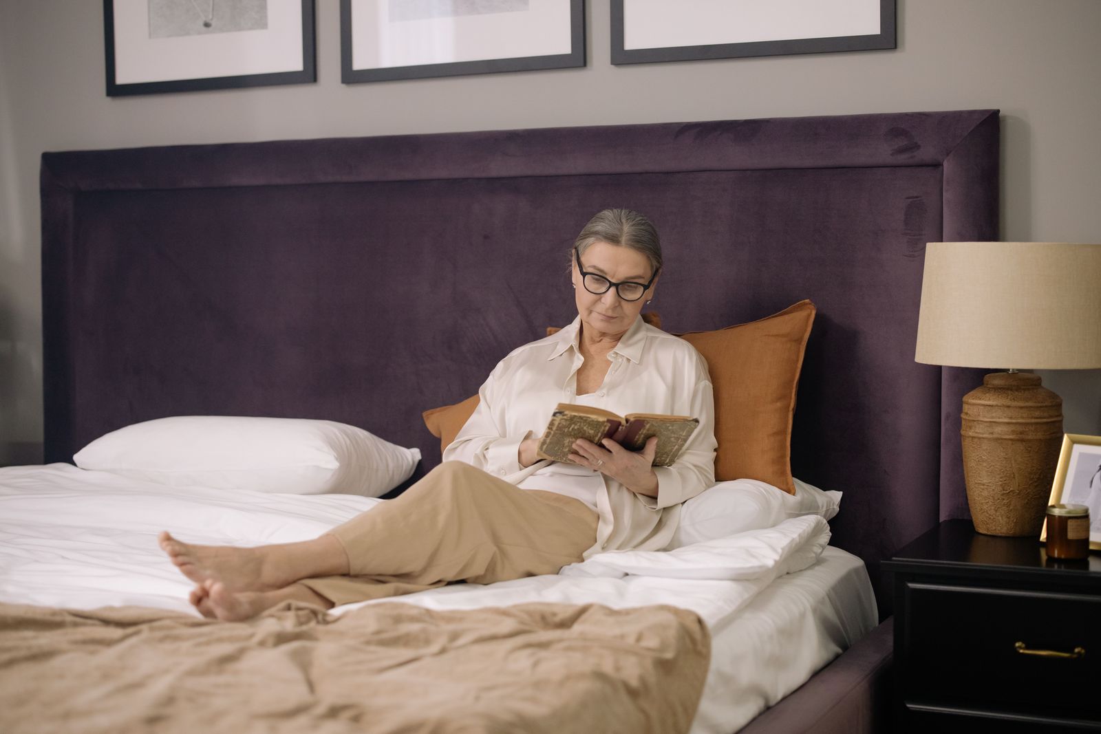Una mujer lee un libro en la cama por la noche, junto a una lámpara de cabecera