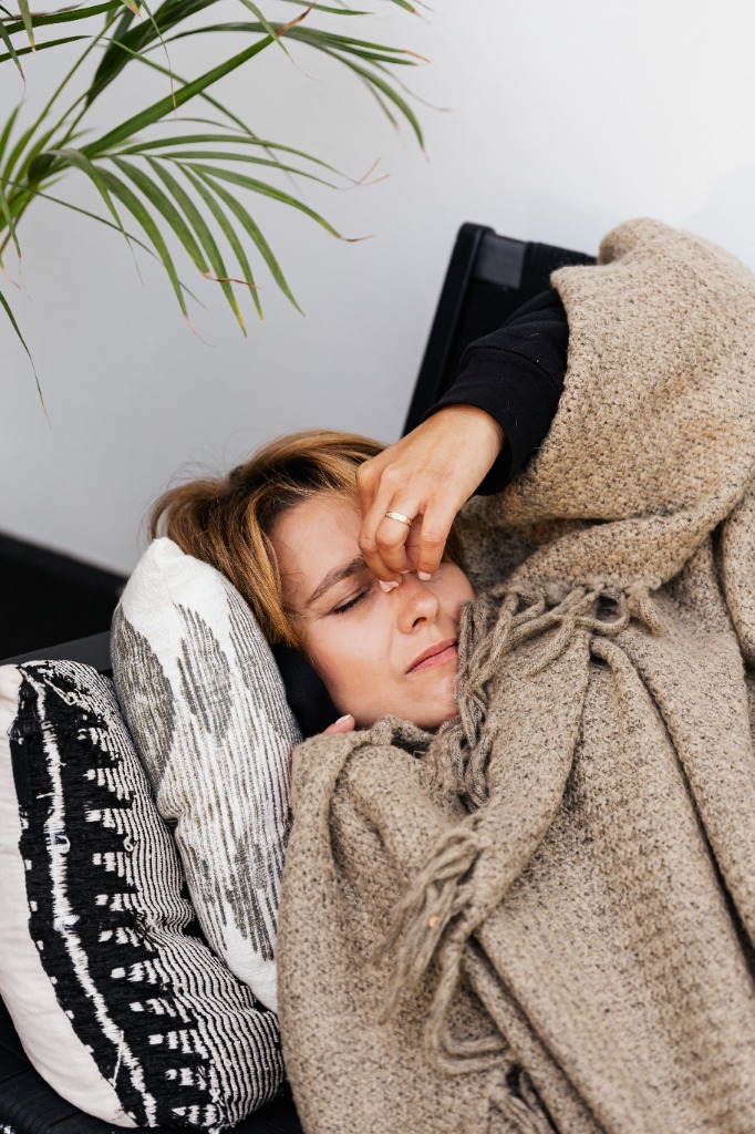 Donna esausta sdraiata sotto una coperta calda e accogliente che tiene la fronte